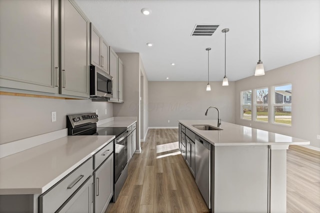 kitchen with sink, decorative light fixtures, gray cabinets, a center island with sink, and appliances with stainless steel finishes