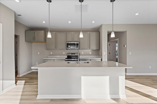 kitchen with appliances with stainless steel finishes, an island with sink, hanging light fixtures, and sink