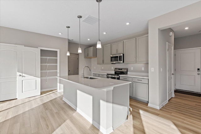 kitchen with light wood-type flooring, gray cabinetry, stainless steel appliances, sink, and an island with sink