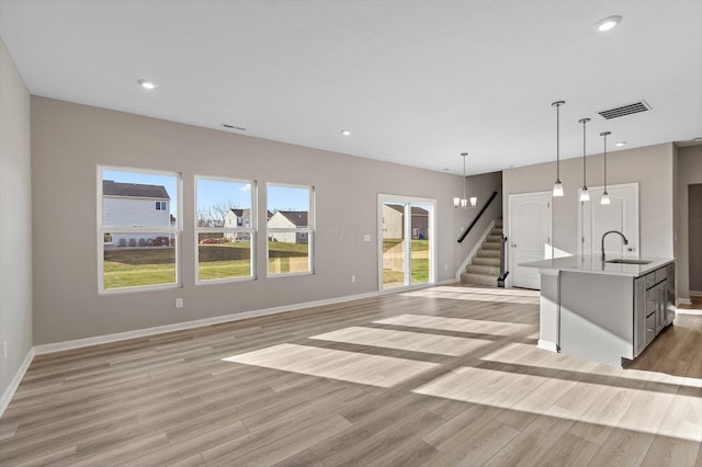 unfurnished living room with light hardwood / wood-style floors, a notable chandelier, and sink