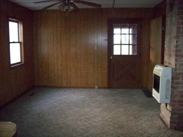 unfurnished living room with heating unit, ceiling fan, plenty of natural light, and carpet