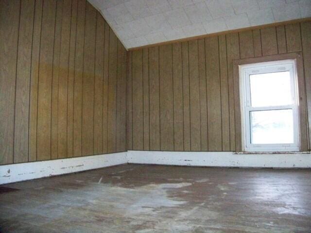 unfurnished room with wooden walls, wood-type flooring, and vaulted ceiling