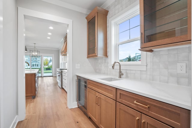 kitchen with sink, crown molding, light hardwood / wood-style flooring, tasteful backsplash, and beverage cooler