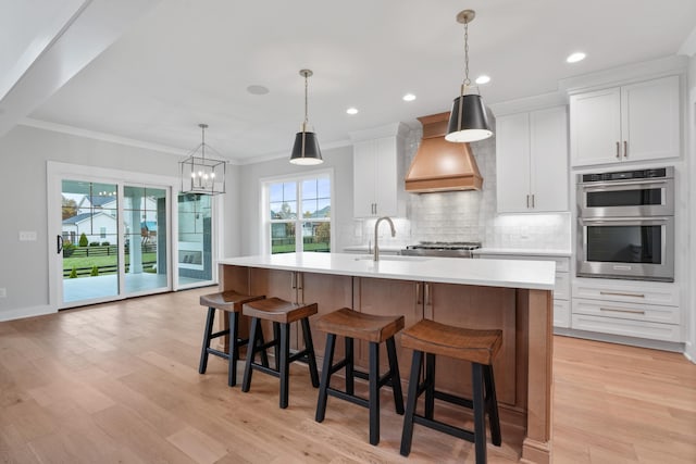 kitchen featuring premium range hood, a large island with sink, white cabinets, sink, and light wood-type flooring