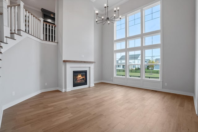 unfurnished living room featuring a chandelier, a towering ceiling, light hardwood / wood-style floors, and ornamental molding