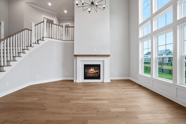 unfurnished living room with an inviting chandelier, ornamental molding, a high ceiling, and light hardwood / wood-style flooring