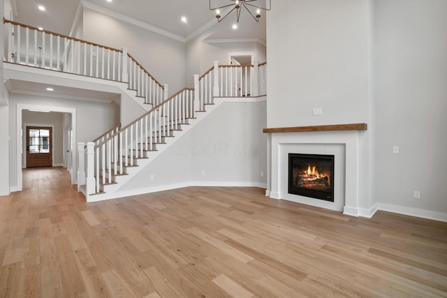 unfurnished living room featuring crown molding, light hardwood / wood-style flooring, a towering ceiling, and an inviting chandelier