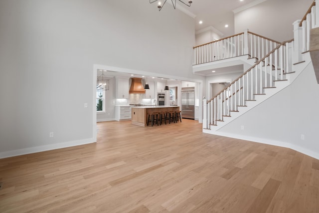 unfurnished living room featuring a high ceiling, sink, crown molding, light hardwood / wood-style flooring, and a chandelier