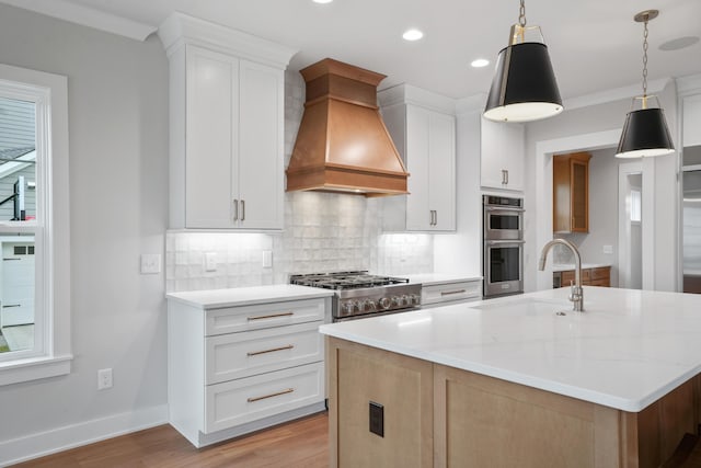 kitchen featuring premium range hood, a kitchen island with sink, white cabinets, hanging light fixtures, and sink