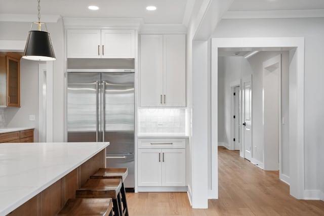 kitchen featuring pendant lighting, white cabinets, built in refrigerator, light hardwood / wood-style floors, and light stone counters