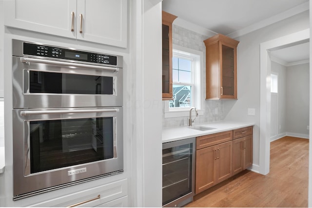 kitchen featuring sink, ornamental molding, light hardwood / wood-style floors, stainless steel double oven, and beverage cooler