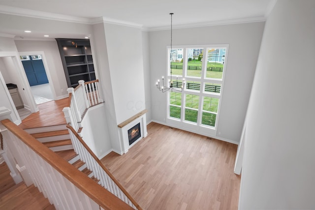 staircase featuring wood-type flooring, crown molding, and an inviting chandelier