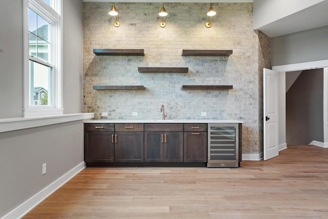 bar with wine cooler, a wealth of natural light, dark brown cabinets, and light hardwood / wood-style flooring