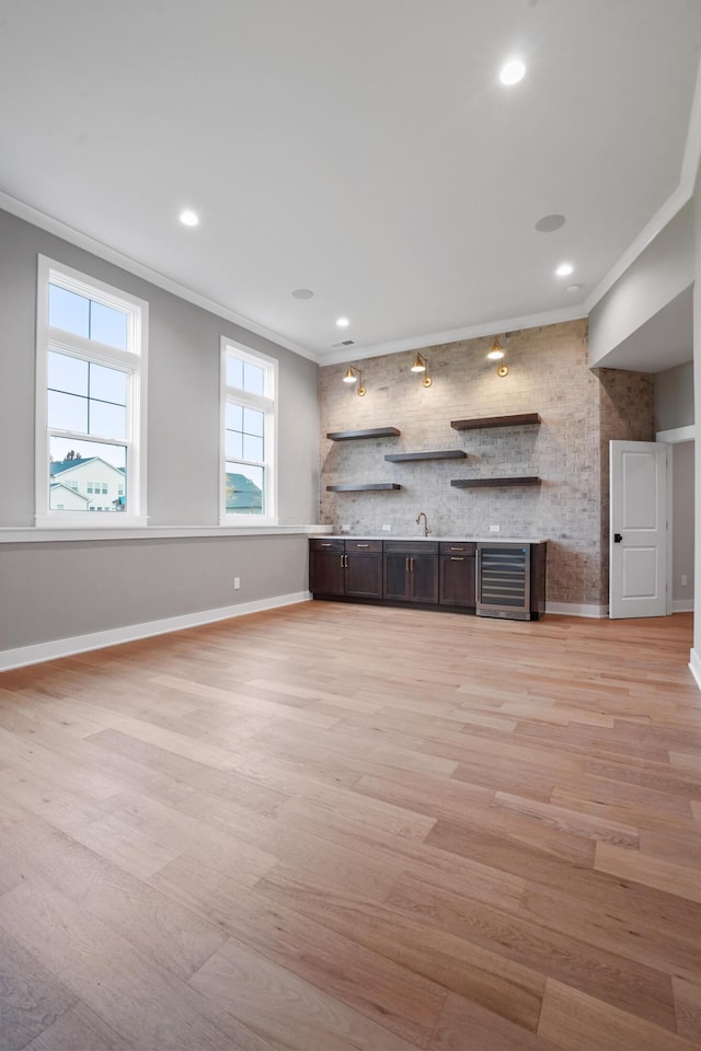 unfurnished living room with light wood-type flooring, wine cooler, and ornamental molding