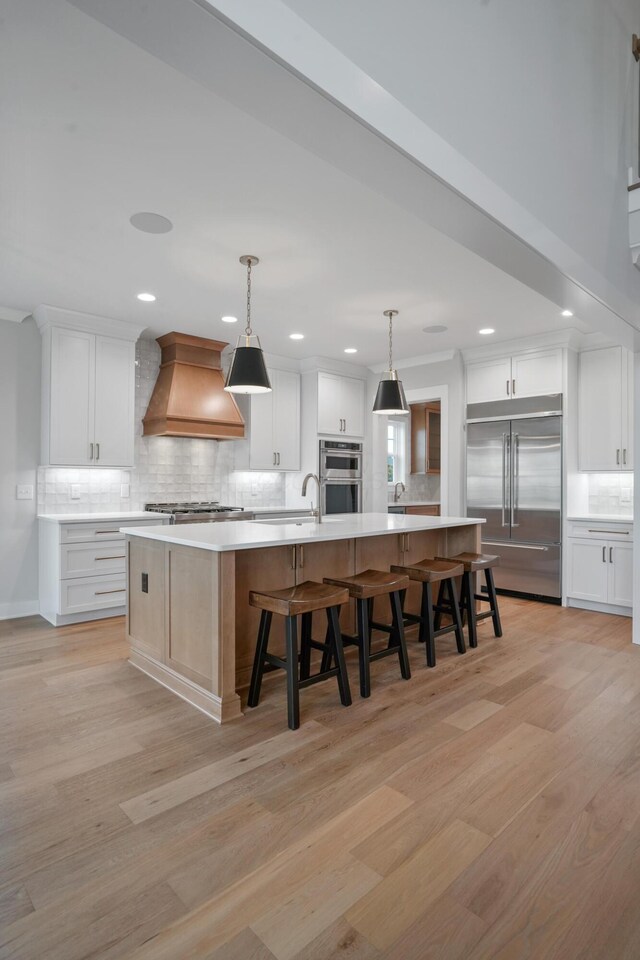 kitchen with appliances with stainless steel finishes, custom exhaust hood, white cabinets, hanging light fixtures, and a large island