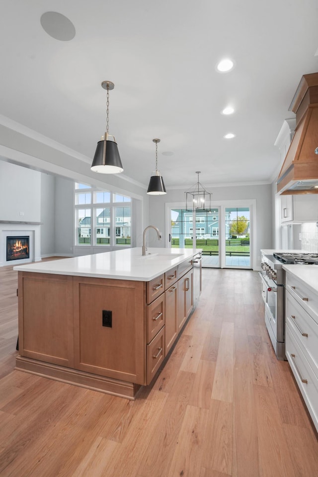 kitchen with white cabinetry, stainless steel range, sink, an island with sink, and pendant lighting