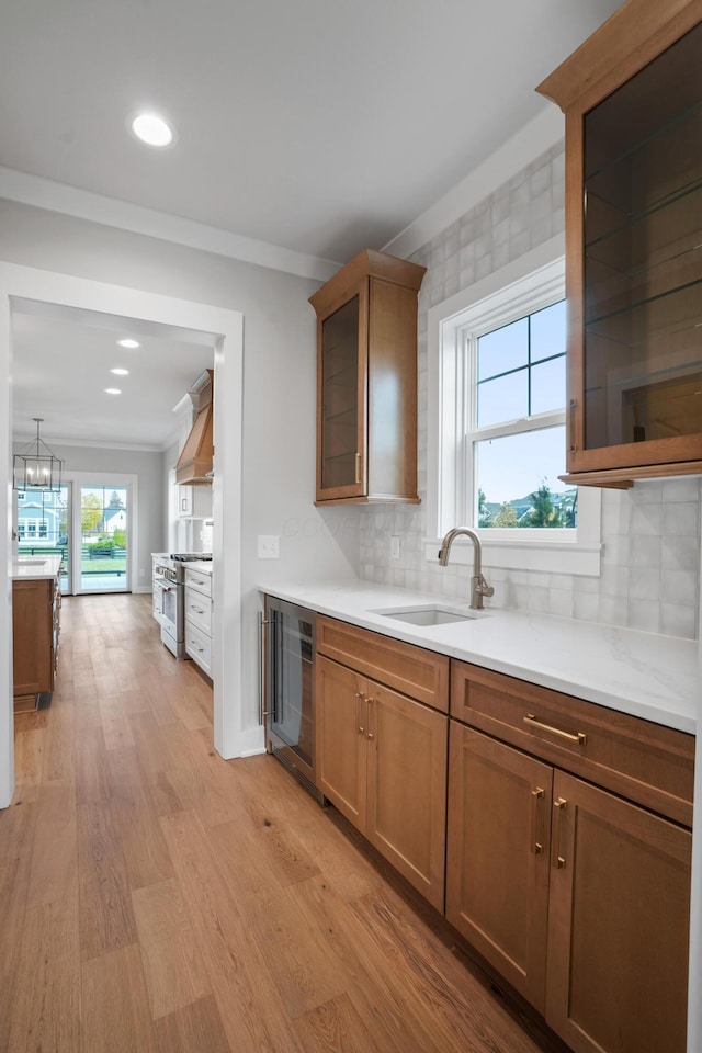 kitchen with tasteful backsplash, custom exhaust hood, beverage cooler, sink, and light hardwood / wood-style floors