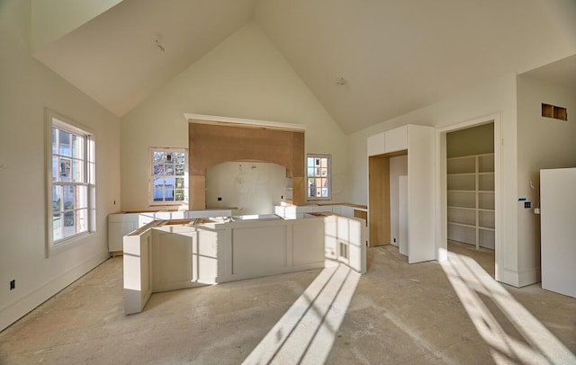 interior space featuring kitchen peninsula, high vaulted ceiling, and white cabinetry