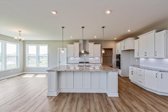 kitchen featuring pendant lighting, wall chimney exhaust hood, and a kitchen island with sink