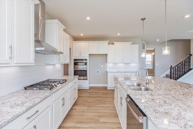 kitchen featuring wall chimney exhaust hood, stainless steel appliances, sink, pendant lighting, and white cabinets