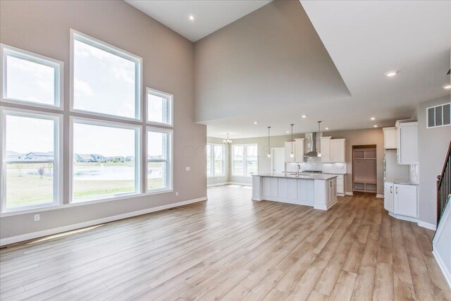 unfurnished living room featuring sink, a towering ceiling, and light hardwood / wood-style floors