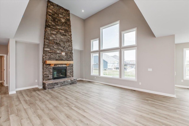 unfurnished living room featuring a stone fireplace, a towering ceiling, and light hardwood / wood-style flooring