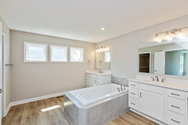 bathroom with hardwood / wood-style floors, vanity, and tiled tub