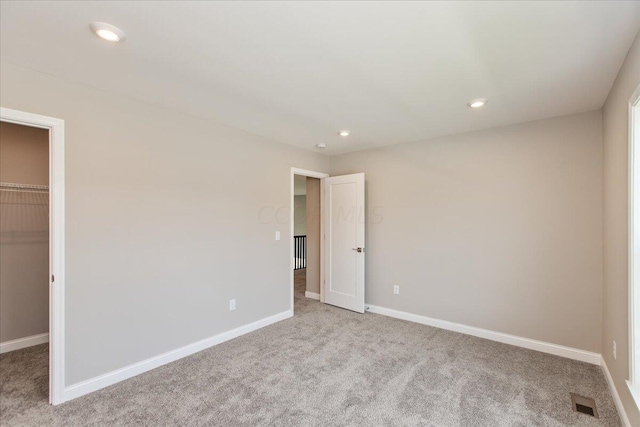 unfurnished bedroom featuring a walk in closet, light colored carpet, and a closet