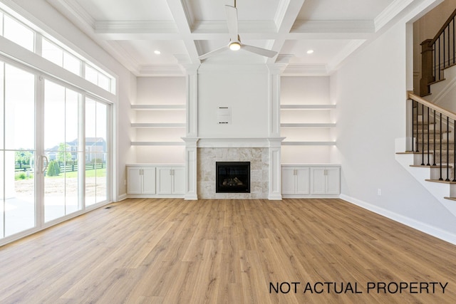 unfurnished living room with beam ceiling, plenty of natural light, a high end fireplace, and light wood-type flooring