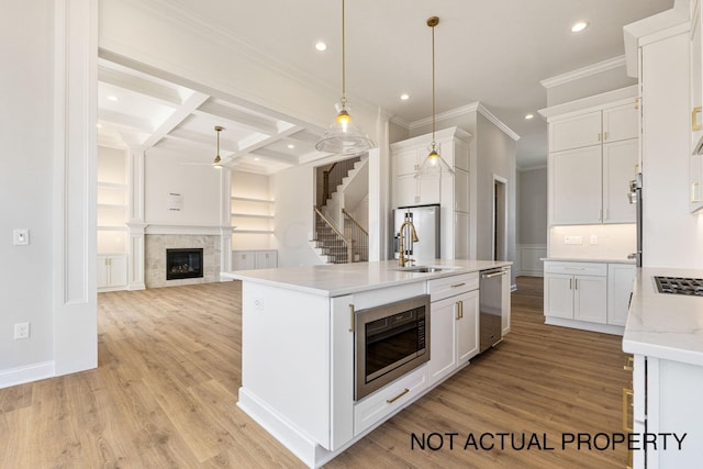 kitchen featuring pendant lighting, coffered ceiling, an island with sink, appliances with stainless steel finishes, and white cabinetry