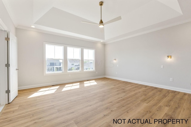 empty room with a tray ceiling, ceiling fan, ornamental molding, and light wood-type flooring