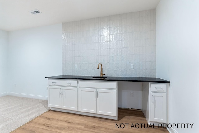 kitchen with tasteful backsplash, white cabinetry, sink, and light hardwood / wood-style flooring