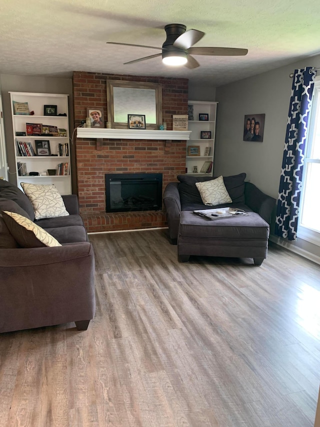 living room featuring a brick fireplace, ceiling fan, a textured ceiling, and hardwood / wood-style flooring