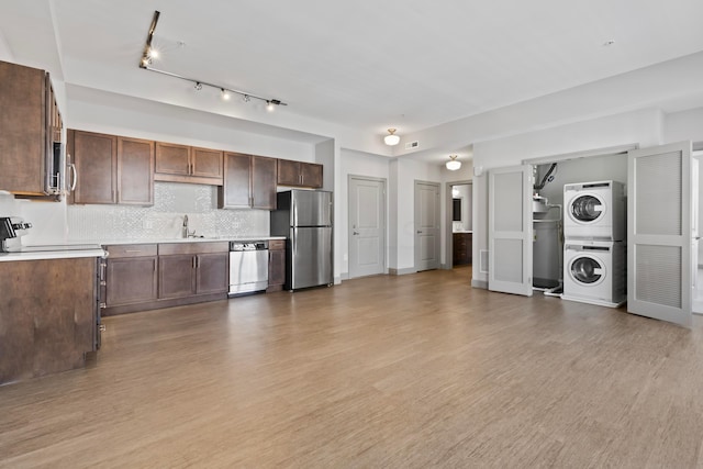 kitchen featuring decorative backsplash, stainless steel appliances, stacked washer / drying machine, and light hardwood / wood-style floors