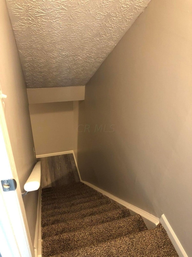 staircase featuring vaulted ceiling, carpet floors, and a textured ceiling