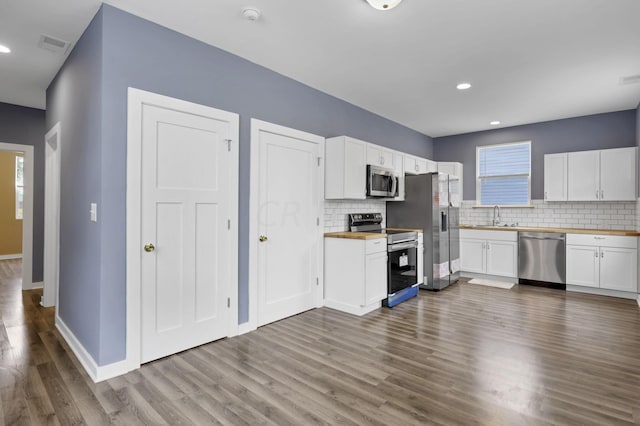 kitchen featuring hardwood / wood-style floors, butcher block counters, white cabinetry, and appliances with stainless steel finishes