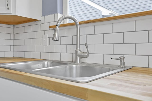 interior details featuring backsplash, sink, white cabinets, and wood counters