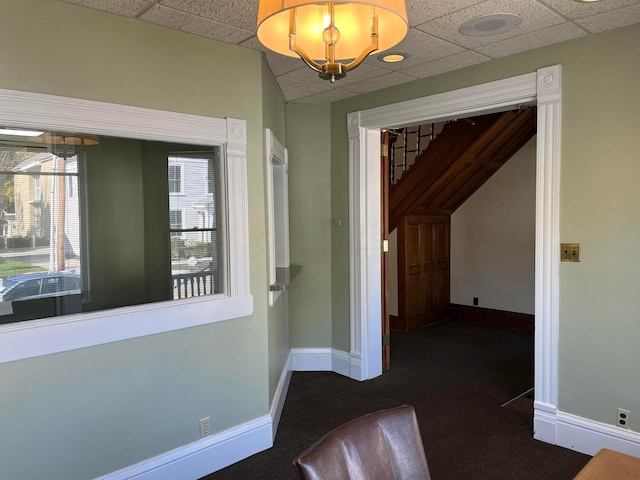 hallway featuring a drop ceiling and dark carpet