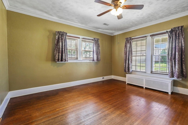 spare room featuring radiator heating unit, dark hardwood / wood-style flooring, ornamental molding, and a healthy amount of sunlight