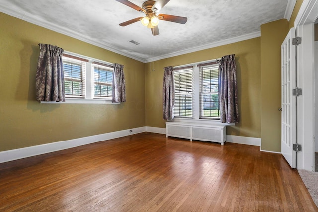 spare room with hardwood / wood-style floors, radiator heating unit, crown molding, and a wealth of natural light