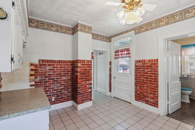 foyer entrance with crown molding, ceiling fan, a healthy amount of sunlight, and brick wall