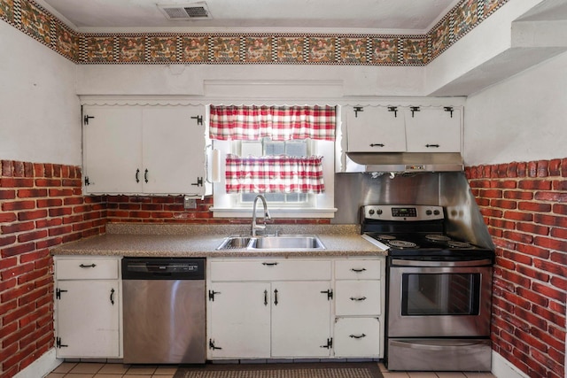 kitchen featuring white cabinetry, sink, brick wall, light tile patterned flooring, and appliances with stainless steel finishes