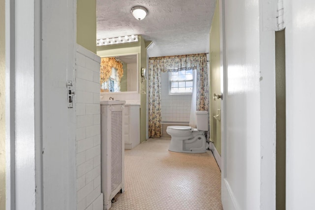 full bathroom with shower / bath combo, vanity, a textured ceiling, tile walls, and toilet