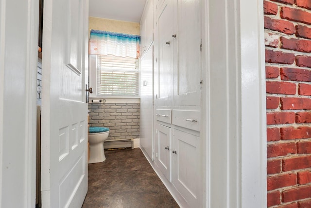 bathroom featuring baseboard heating, brick wall, concrete flooring, and toilet