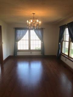 spare room featuring a healthy amount of sunlight, dark wood-type flooring, and a notable chandelier