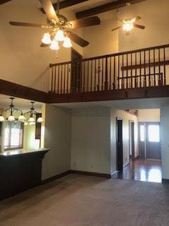 unfurnished living room featuring a high ceiling, a healthy amount of sunlight, and beam ceiling