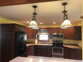 kitchen featuring stainless steel appliances, dark brown cabinetry, and decorative light fixtures