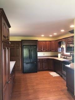 kitchen featuring light wood-type flooring, dark brown cabinets, stove, and black fridge