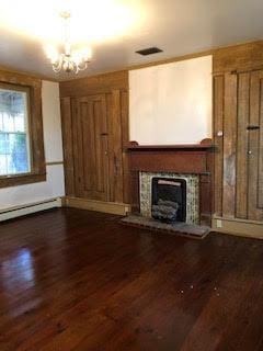 unfurnished living room with a baseboard radiator, a tile fireplace, dark hardwood / wood-style floors, and a chandelier