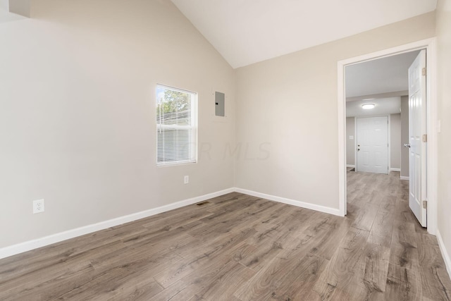 unfurnished room featuring electric panel, vaulted ceiling, and light wood-type flooring